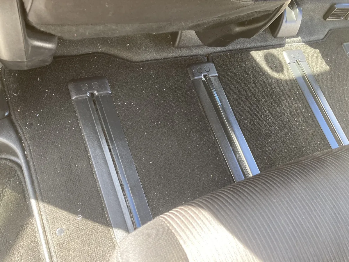 施工前の2列目足元。マットとシートレールのまわりに白い糸くずやホコリが散らばっている状態(島根県出雲市・日産セレナ)