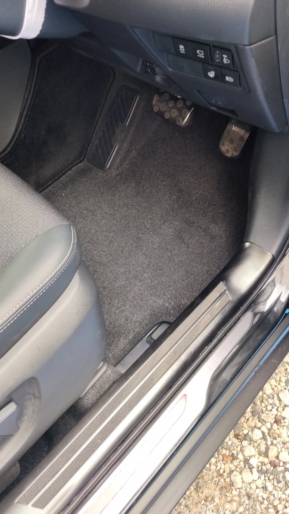 トヨタ ヤリスクロスの施工前。運転席のドアを開けて足元とステップを写した写真で、手前にステップの樹脂とスカッフプレート、奥にペダルが見えている
