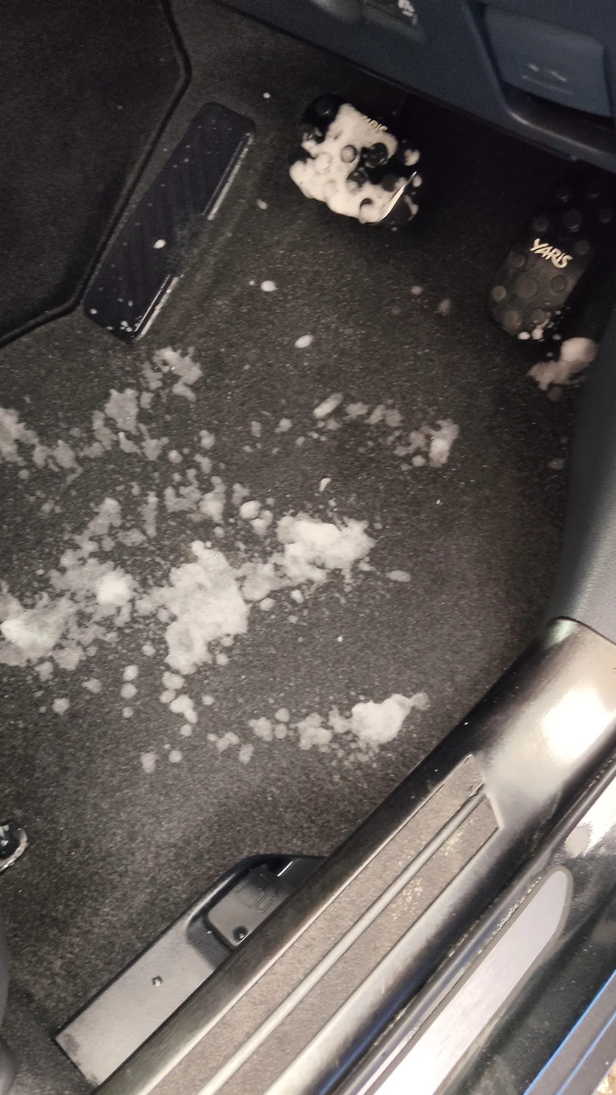 トヨタ ヤリスクロスの施工中。運転席の足元に白い泡が点々と乗っており、奥にペダルが見えている