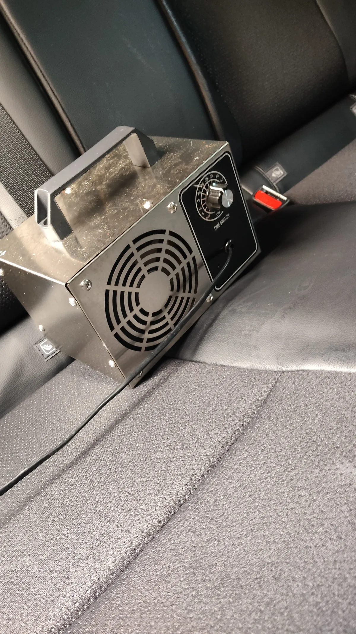 トヨタ ヤリスクロスの施工中。後部座席の上に置かれたステンレスの箱型の機械で、正面にファンの丸い格子と、TIME SWITCHと書かれたタイマーのダイヤルが付いている