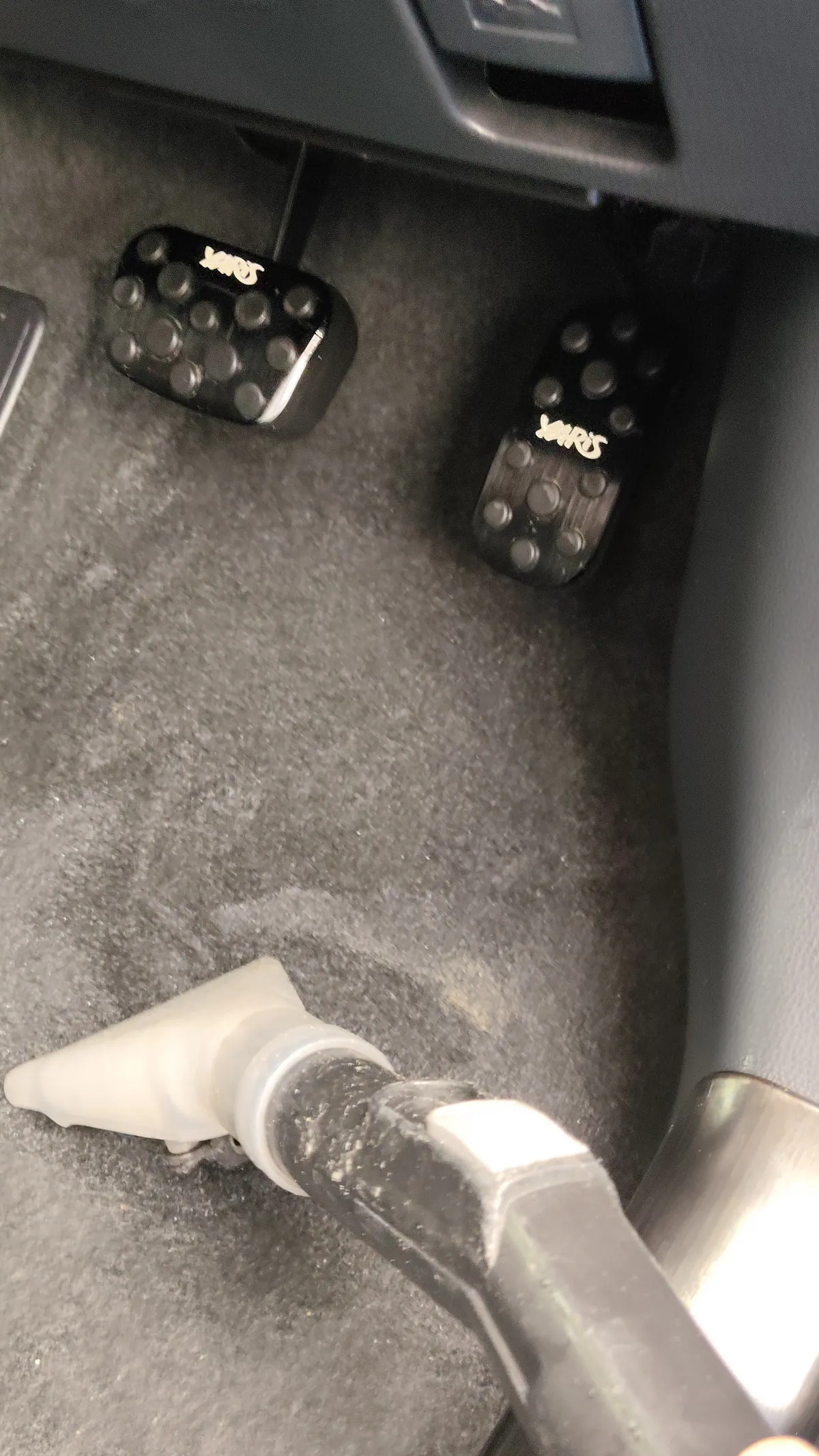 トヨタ ヤリスクロスの施工中。運転席の足元のカーペットに、透明樹脂の三角形のノズルを当てている。奥にペダルが2つ見えている
