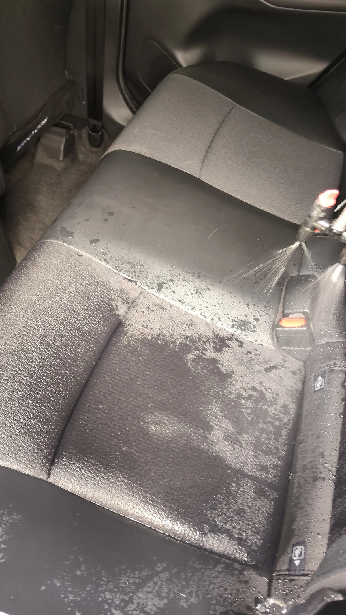 トヨタ ヤリスクロスの施工中。後部座席の座面に向けてノズルから洗浄液を噴射しており、座面が濡れて色が濃くなっている