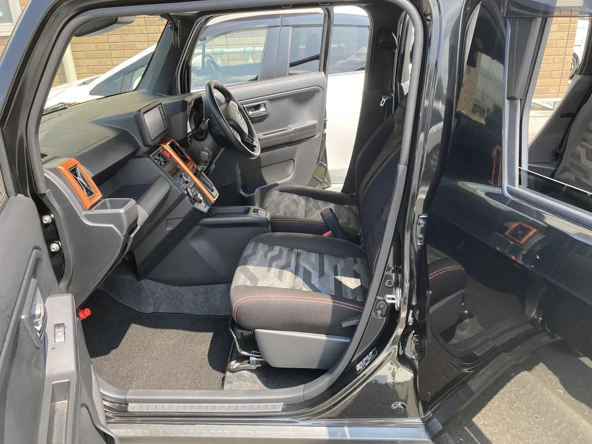 ダイハツ タフトの車内を助手席側から見たところ。ステアリングとダッシュボード、オレンジ色のアクセントパネル、助手席の座面、黒いフロアマットが写っている