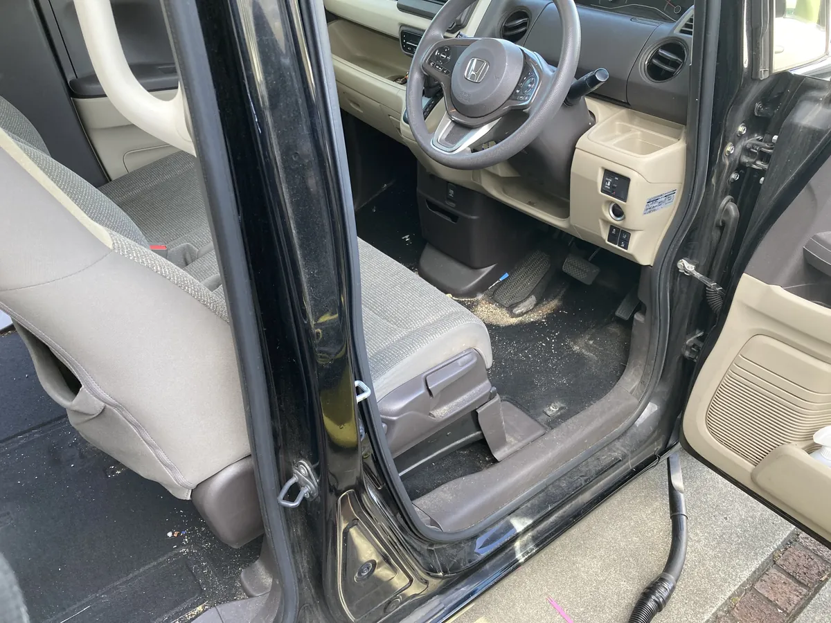 ホンダ N-BOXの運転席側のドアを開けたところ。奥にステアリングとダッシュボード、手前に運転席のシートが写り、黒いフロアカーペットの上にペダルの付け根に沿って黄土色の粒が帯状に溜まり、白っぽい細かい粒が全面に散っている