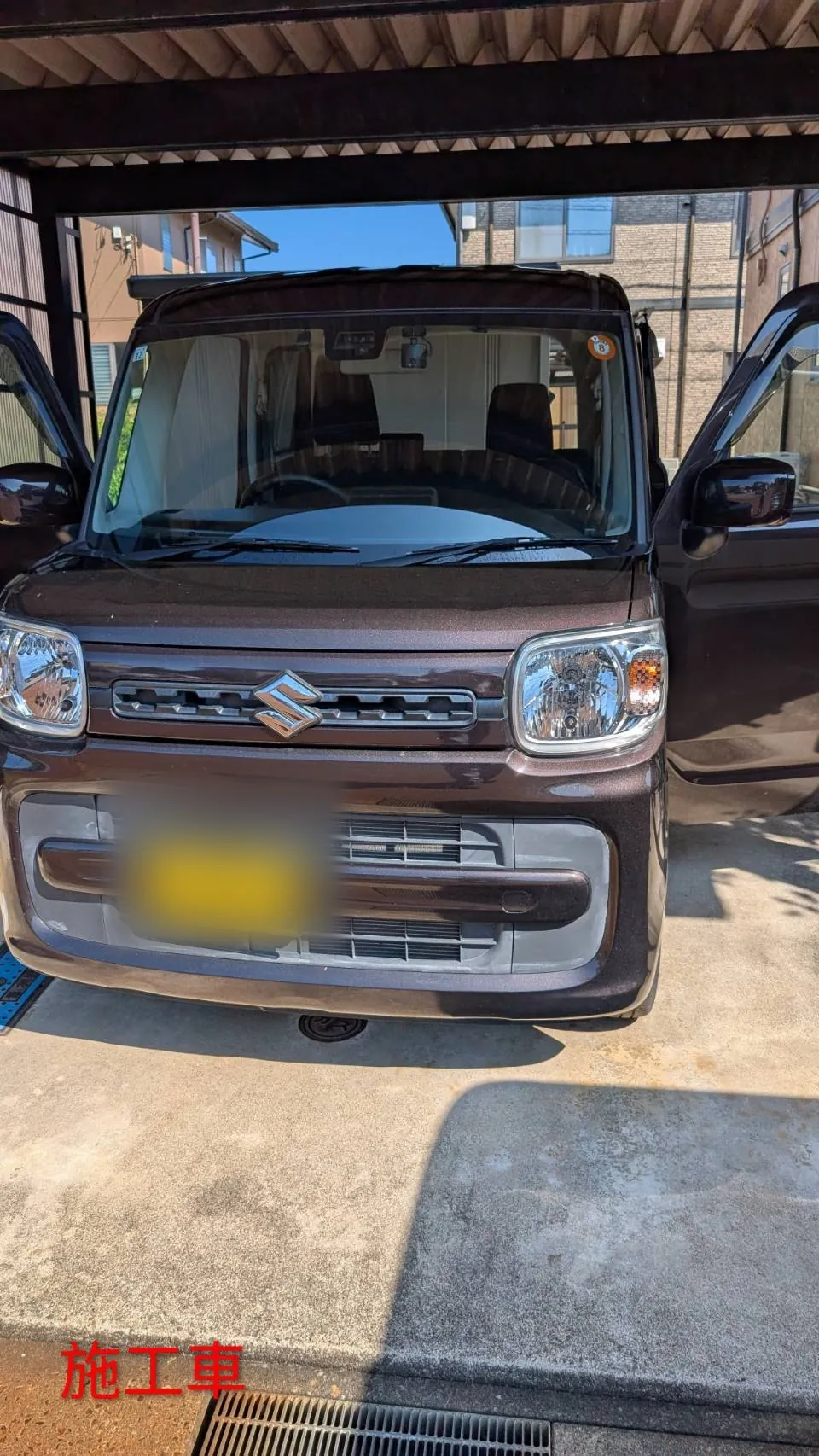 施工車のスズキ スペーシア。こげ茶色の車体を前から見たところで、フロントグリルにスズキのエンブレムが付いている