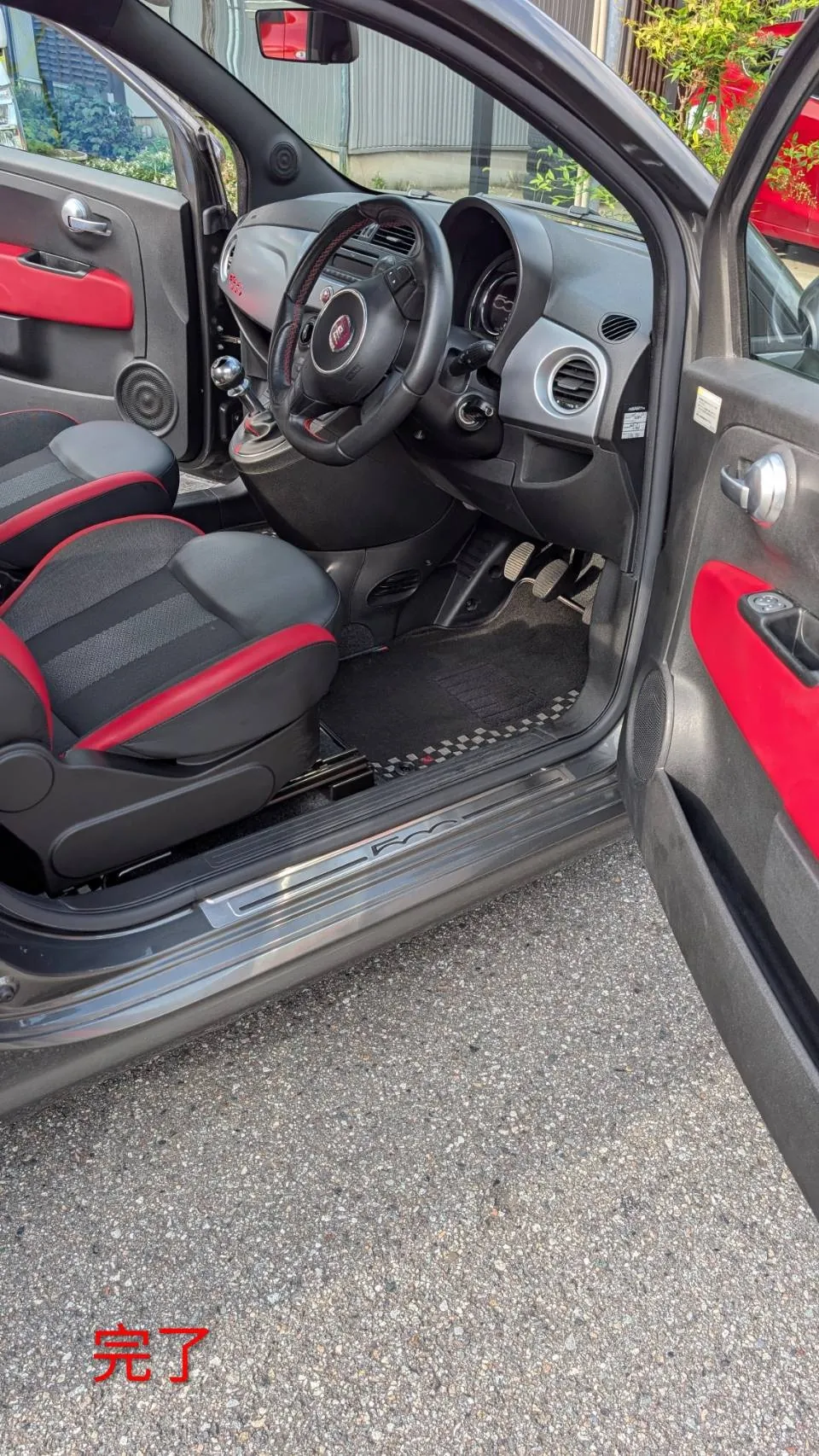完了後のFIAT 500Sの車内。運転席側のドアを開けた状態で、ステアリング、ペダル、赤い内張りのドアが見える
