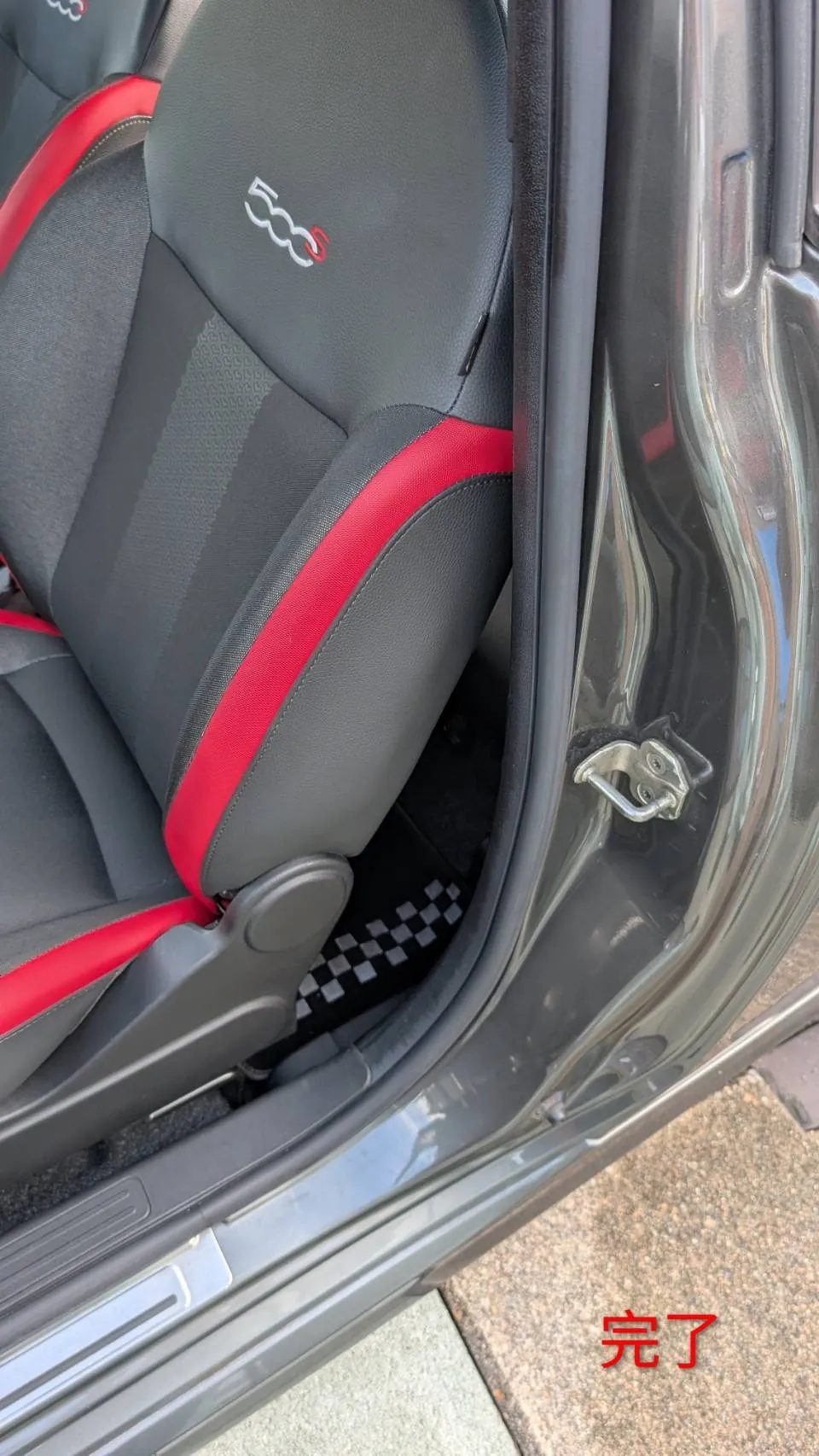 完了後のFIAT 500Sの助手席シート。500Sのロゴと赤いパイピングが入った布地の座面と背もたれ、開いたドアの開口部が見える