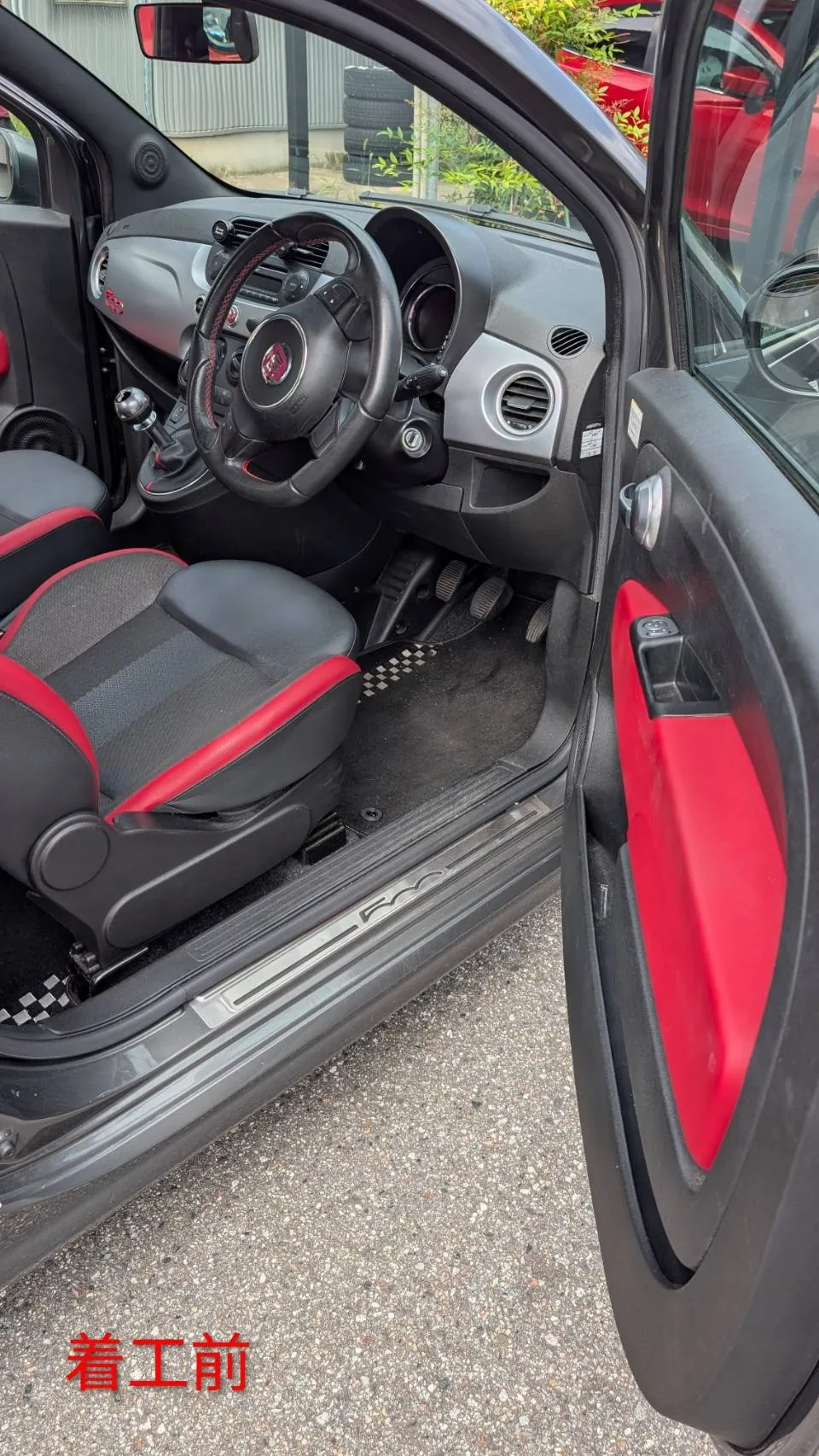 着工前のFIAT 500Sの車内。運転席側のドアを開けた状態で、ステアリング、ペダル、赤い内張りのドア、シフトレバーが見え、奥に助手席がある