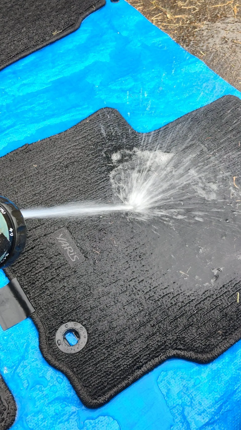 外したフロアマットを青いシートの上に置いて水をかけている