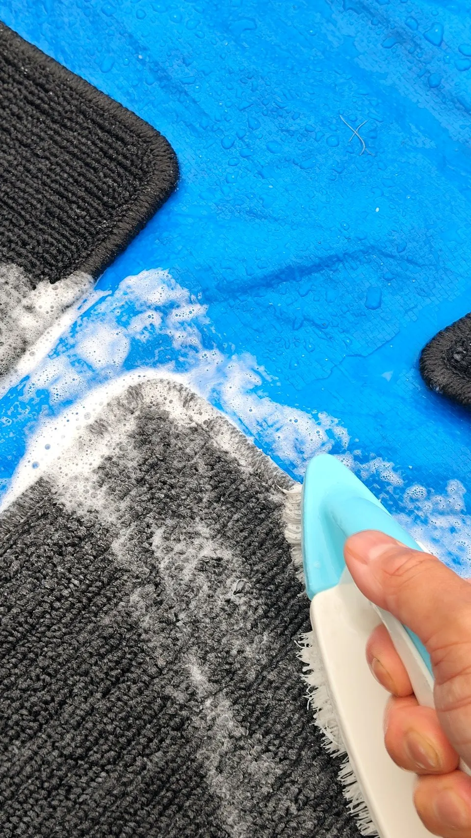 青いシートの上で、水色のブラシを手に持ってマットをこすっている。白い泡が立っている