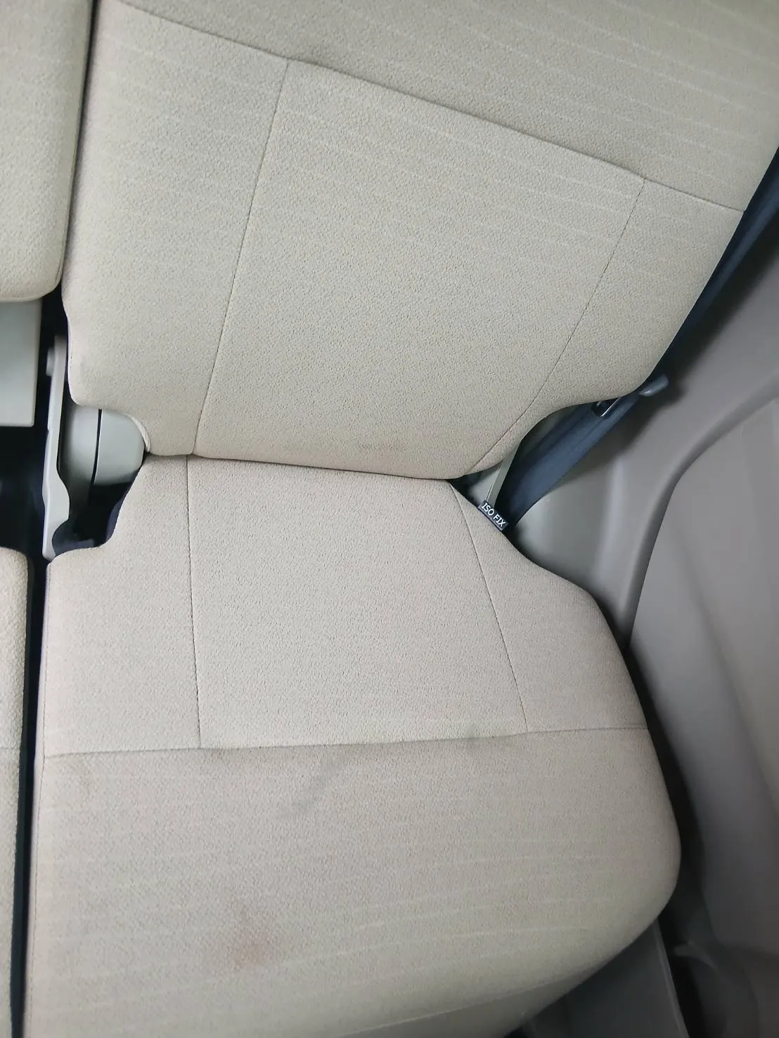ダイハツ ムーヴのシートの座面に寄った一枚。ベージュの布地とISO FIXのタグ、縦に細く伸びた濃淡