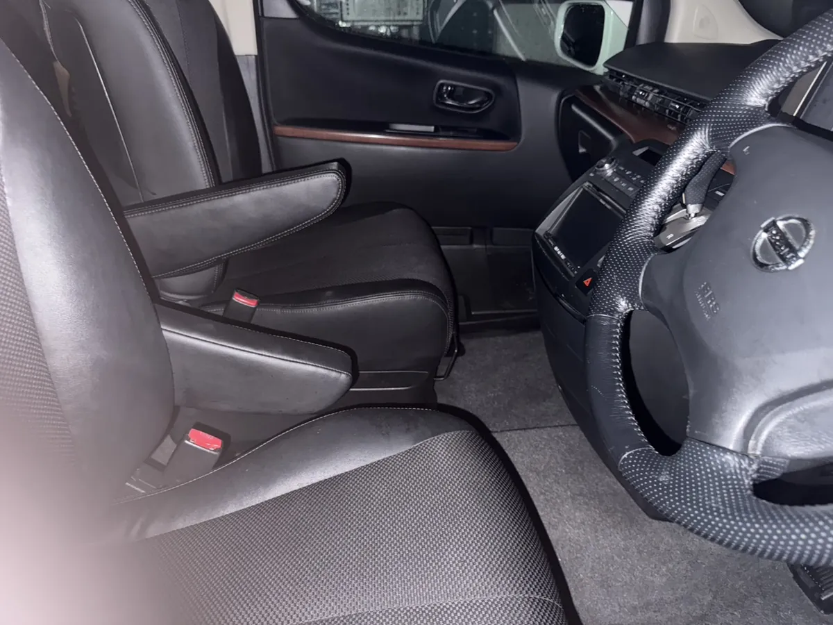 作業を終えた日産エルグランドの運転席まわり。黒い革巻きのステアリングに日産のエンブレム、中央が織り目のある生地の黒いシート、木目調の内張りパネルが写っている。