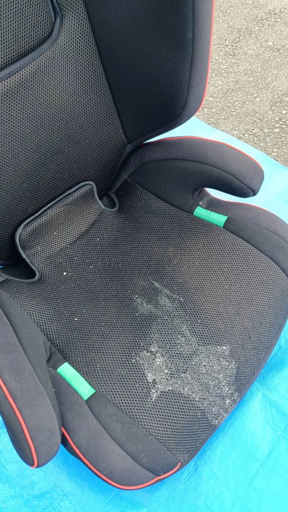 作業前のチャイルドシート。車外の青いシートの上に置かれ、黒いメッシュ地の座面に吐いてしまったものが広く付いている
