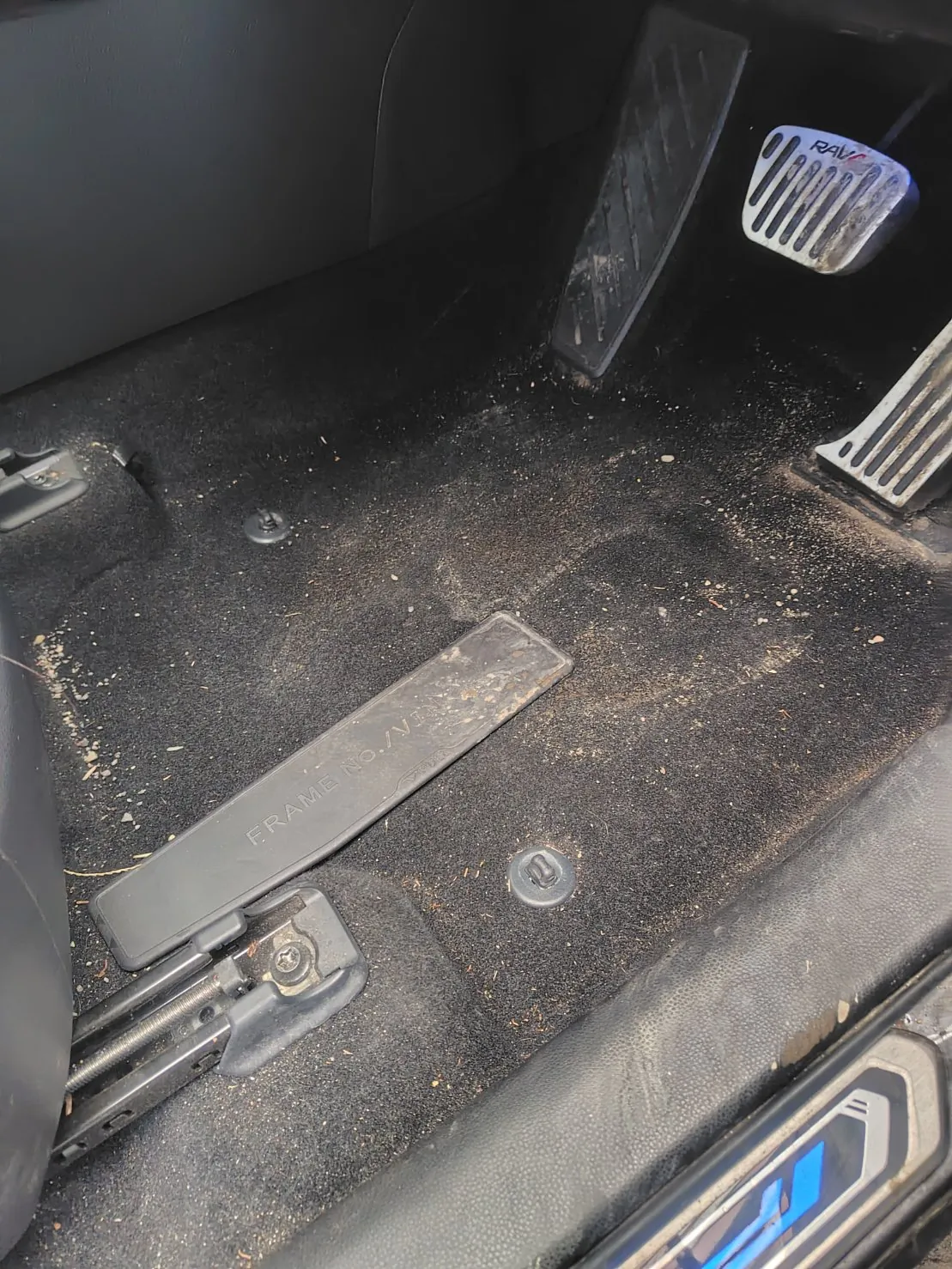 作業前の運転席の足元。黒い起毛のカーペットに白い小石と砂、枯れ草が散っている