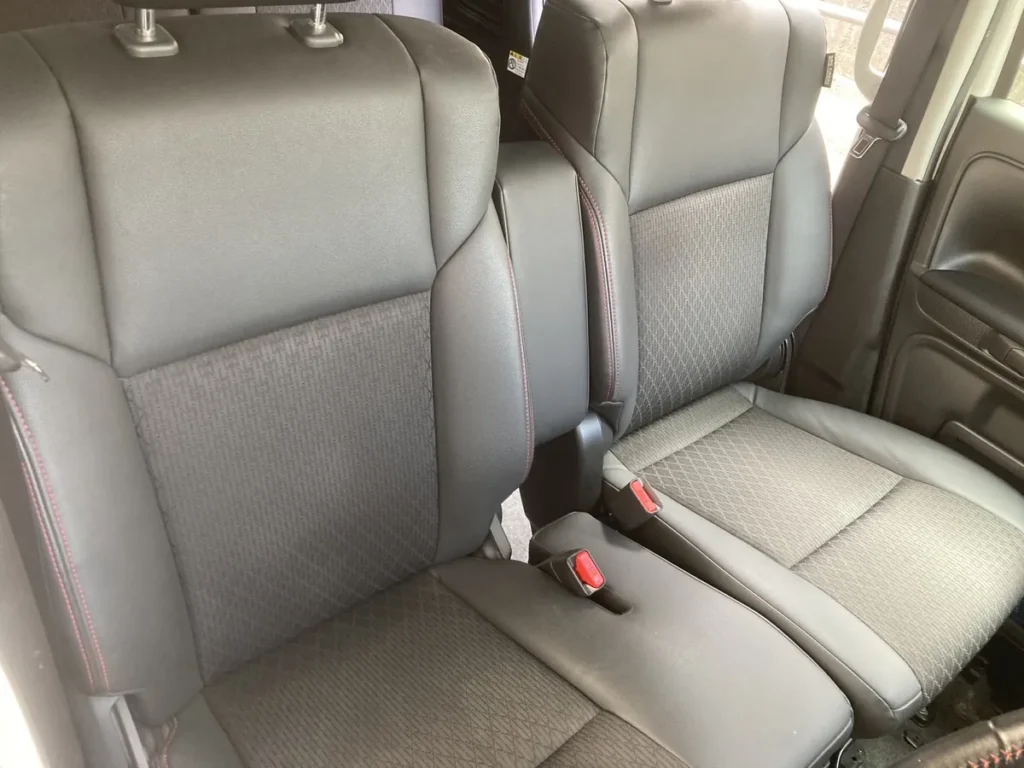 作業後のスズキ スペーシアの後部座席を、車内側から撮ったところ。手前に背もたれの前面があり、上端にヘッドレストの支柱が2本見えている。奥の席に細かい格子の織りの座面と、赤いボタンの付いたシートベルトのバックルが写っている
