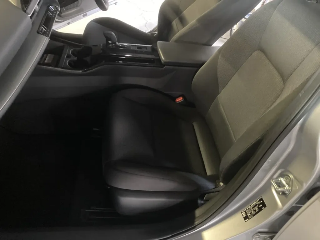 作業後のトヨタ プリウスの助手席。背もたれはグレーの布、座面は黒。座面の奥に赤いボタンの付いたシートベルトのバックル、左にシフトレバーとカップホルダーの並んだセンターコンソール。足元の床は黒