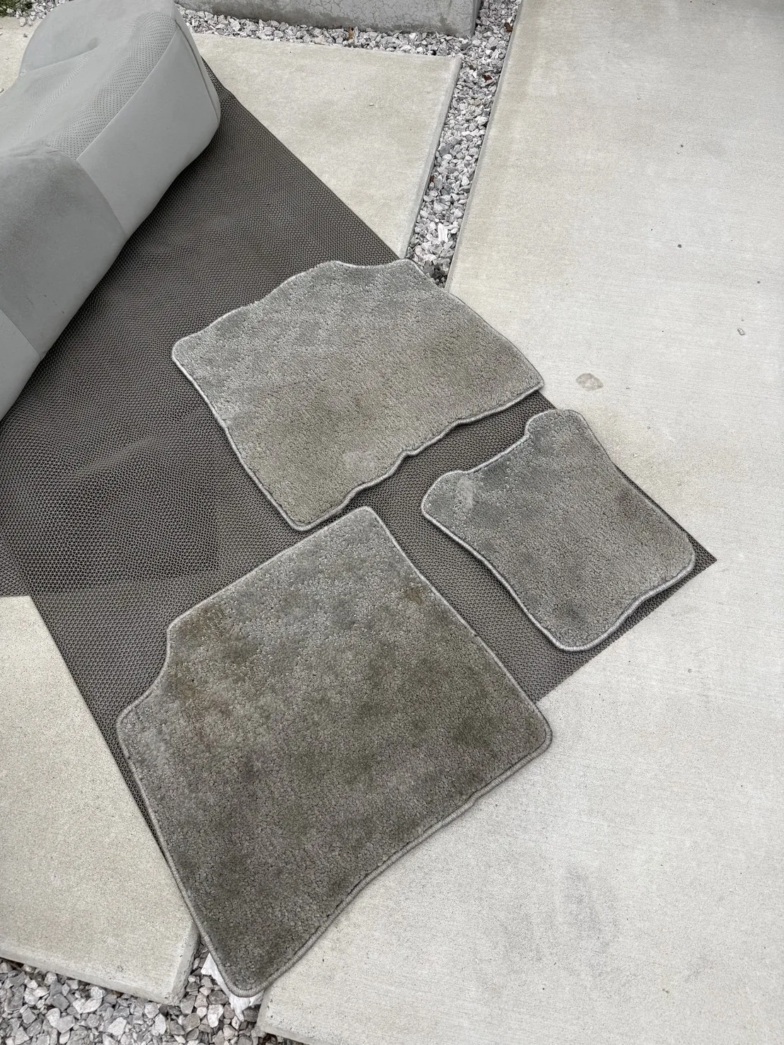 黒いメッシュマットの上に並べたフロアマット3枚。手前の1枚が広く茶色く変色している作業前の様子
