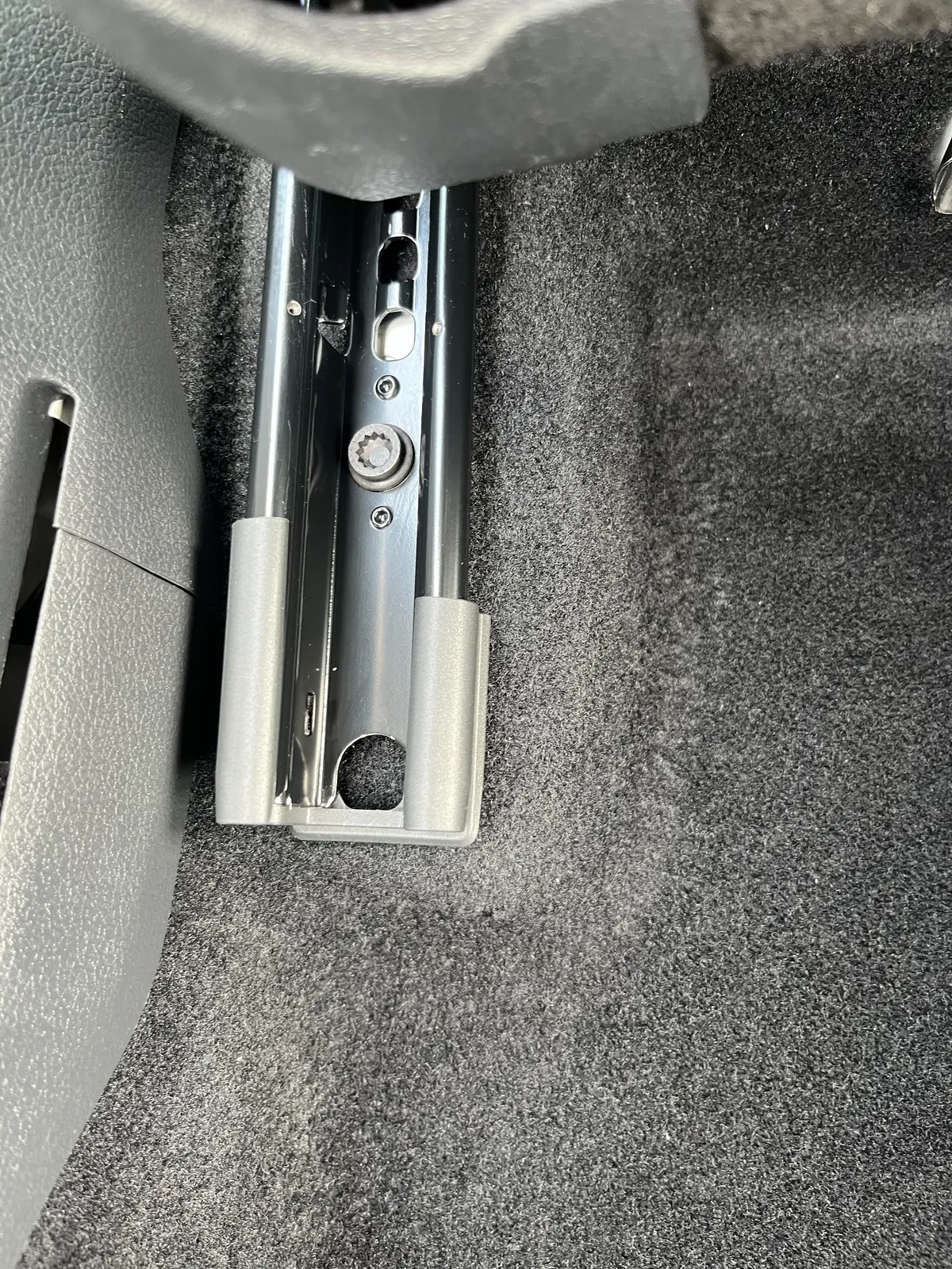 同じシートレールのまわりの床。カーペットに砂やほこり、毛が見当たらず、レールの金属の面が出ている