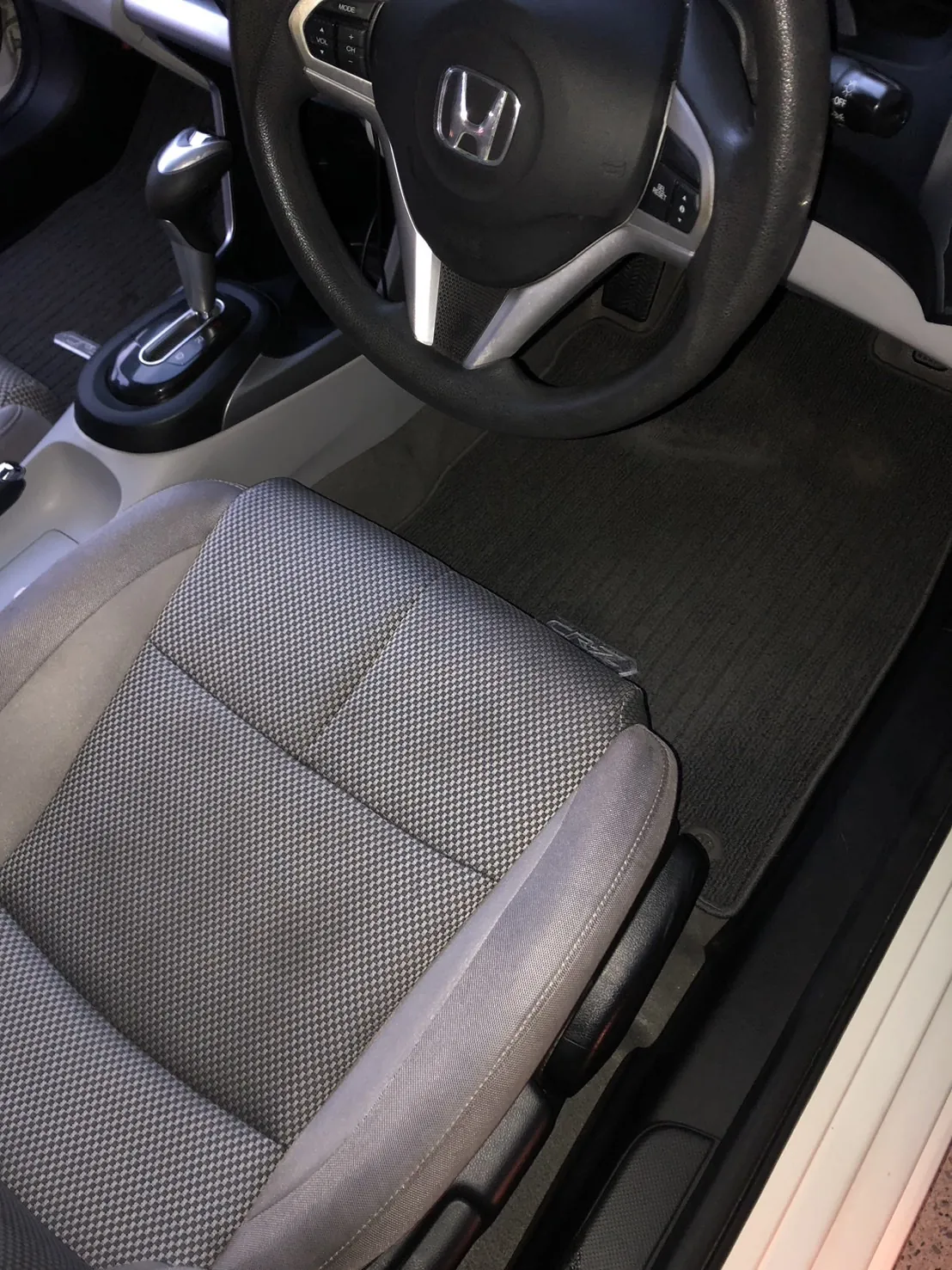 作業後のホンダ CR-Zの運転席まわり。運転席のドアを開けて外から撮ったところ。上にホンダのエンブレムの付いたステアリング、左にシフトレバーとオートマのセレクター、手前に運転席の座面、右に黒いフロアマットが広く写っている