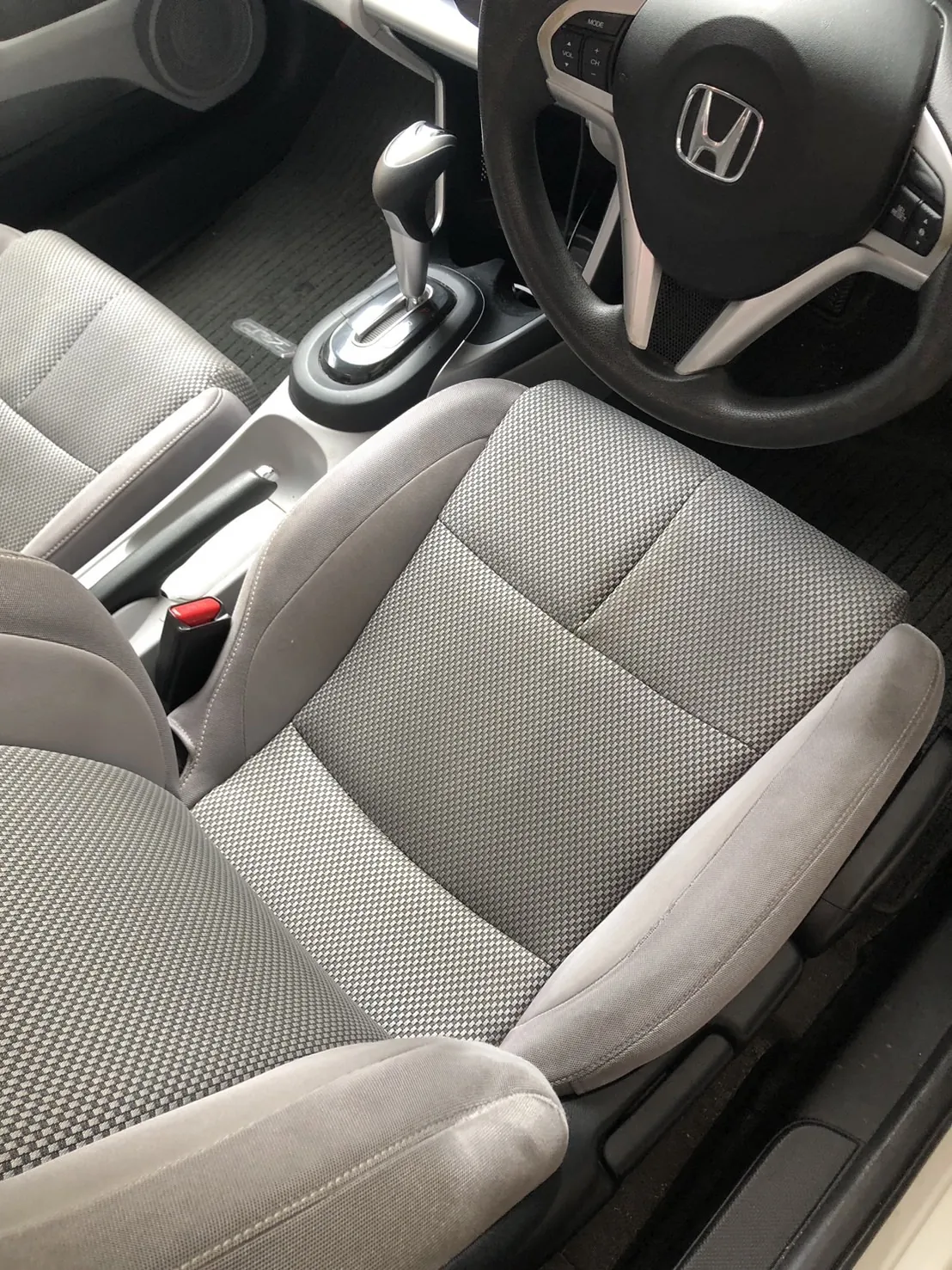 作業前のホンダ CR-Zの運転席まわり。ホンダのエンブレムの付いたステアリング、シルバーのシフトレバーとオートマのセレクターが写り、手前に運転席の座面が大きく入っている。座面の中央はグレーの市松模様の織り、左右は濃いグレーの起毛の切り替え