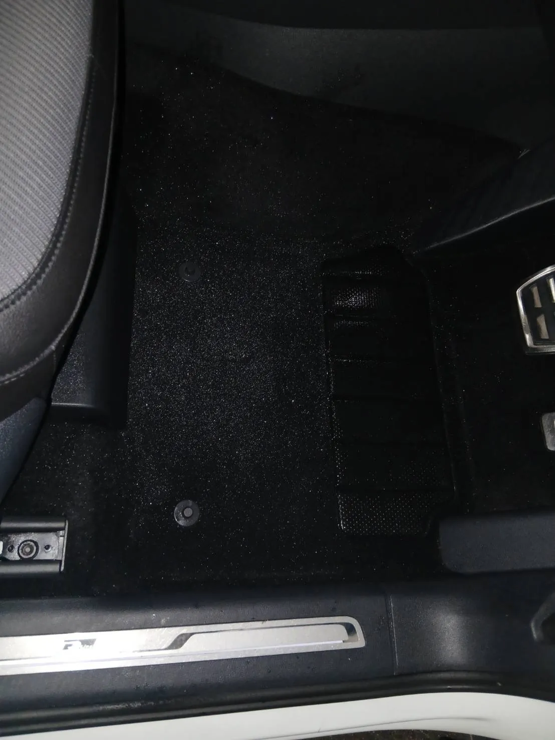 フロアマットを戻した運転席の足元。黒いマットと留め具、ステップの銀色のプレートが見えている
