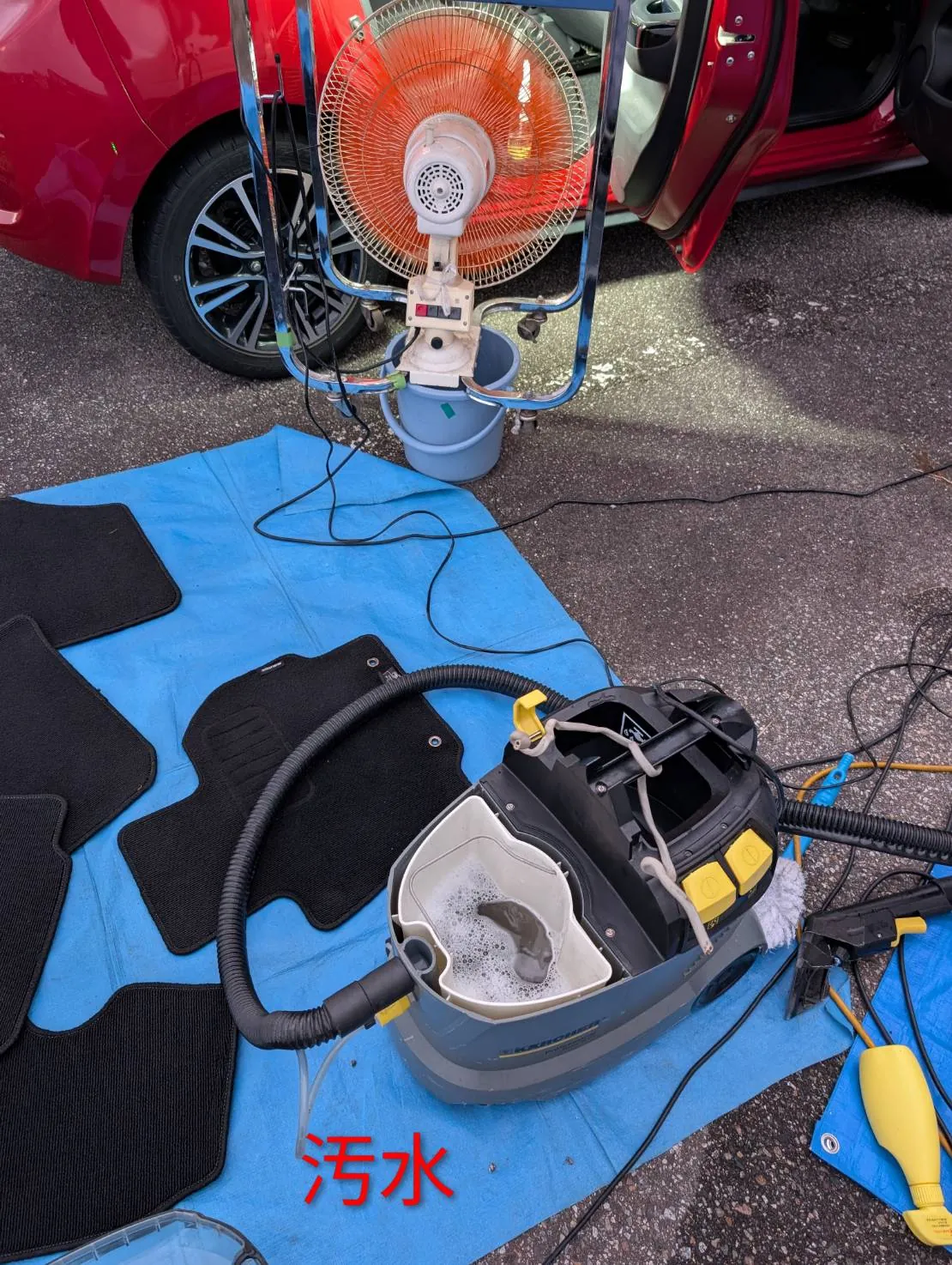 青いシートの上に外したフロアマットが4枚並び、手前に回収タンクの泡立った水が見えている